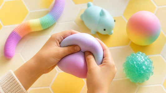 Child's hands squeezing a pastel squishy toy, surrounded by colourful sensory fidget toys on a honeycomb background